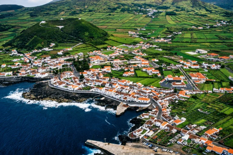 Vista aérea de uma vila costeira na ilha Graciosa, nos Açores, rodeada por campos verdes, associada à maior frequência da Doença Machado-Joseph nas ilhas açorianas.