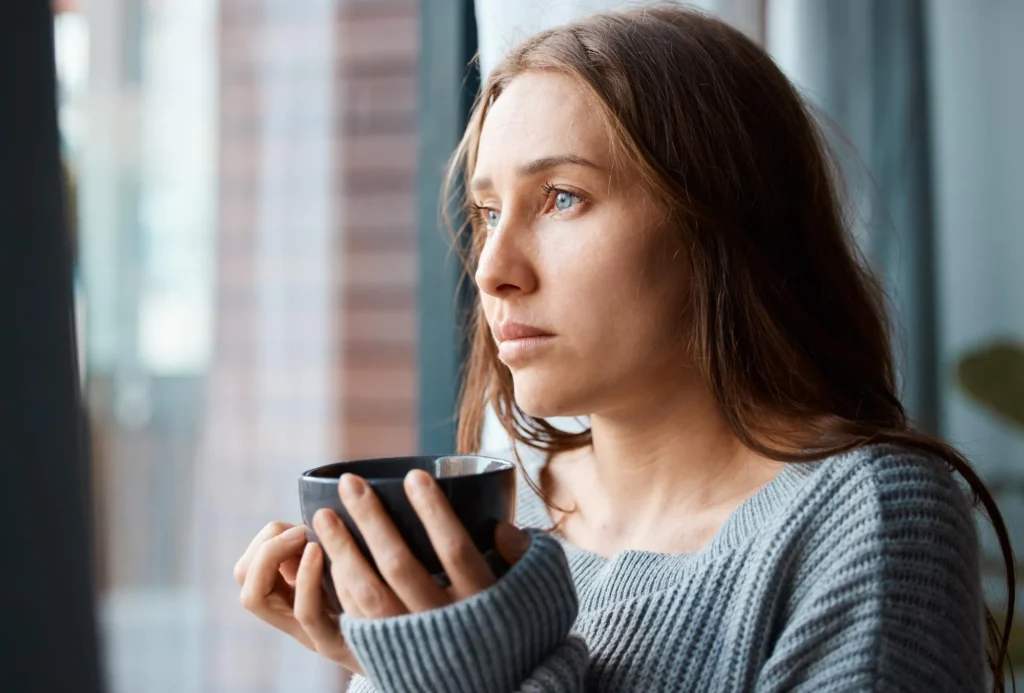 Mulher jovem com expressão ansiosa a segurar uma chávena de café, representando a possível ligação entre cafeína e a criação de um ciclo de ansiedade, palpitações e ataques de pânico.